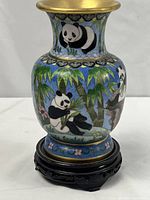 Front view of cloisonne vase showing panda bear motif and bamboo leaves, seated on carved wood stand.