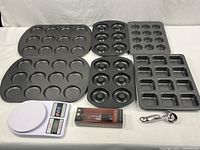 Photo showing the full collection of baking pans, digital scale, silicone brush in box, and measuring spoon on a white backdrop.