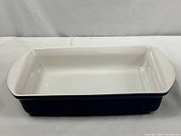 Front and side view of rectangular enamel-coated cast-iron baking dish showing white interior and dark blue exterior.