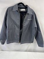 Full front view of the gray jacket hanging on hanger, showing collar and zipper, with "GENERAL AFFAIRS" embroidery visible on left chest.