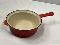 Side view of orange-red enamel Le Creuset cast iron pot with handle, interior visible.