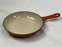 Full view of the red Le Creuset cast-iron shallow fry pan with cream interior enamel, showing its shape and handle.