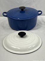 Blue round enameled cast iron Dutch oven with two lids, one blue and one white, displayed on a white surface.