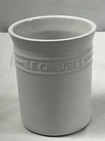 Front side view of large white Le Creuset utensil crock showing embossed logo and smooth finish.