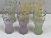 Group of six vintage mid-century modern frosted glass tumblers in pastel colors with floral and bird motifs and gold rims.