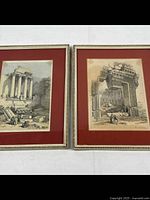 Pair of framed prints showing classical architectural ruins with columns, matted in red and framed in thin gold patterned metal frames.