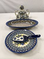 Front left angle view of all items showing overall set including covered jar, oval dish, round plate, and server spatula with blue flower designs