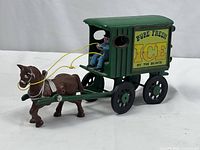 Side view of antique cast iron horse pulling green wagon with yellow signage 'Pure Fresh Ice by the Block'. Shows horse, reins, driver figure, and wagon wheels.