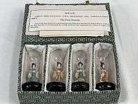Full set of four miniature Asian figurines displayed inside a green patterned box with an informational insert about the four seasons