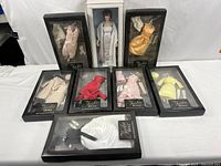 Full view of the Jackie doll standing in white satin gown with seven boxed outfits arranged in front, showing clothing colors and packaging condition.