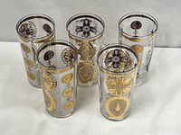 Front view of five clear glass highball glasses with detailed gold and gray ornate floral and circular patterns.