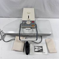 Overview of the Singer Magic Steam Press 7 with accessories: two fabric covers, small black accessory, and instruction manual.