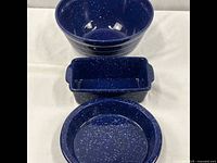 Photo showing all three ceramic dinnerware pieces: a round bowl, a rectangular baking dish with handles, and a pie plate, all blue with white speckles on a light background.