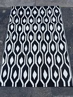 Full view of the outdoor rug showing the white and black geometric pattern on asphalt surface.