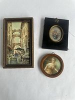 Three vintage picture frames on a white background showing different artwork: city canal, floral bouquet, and portrait of woman.