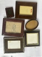 Six assorted small photo frames arranged on a white background. Various shapes include rectangular, square and oval in wood, metal and composite materials.