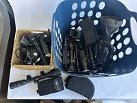Blue laundry-style basket filled with various tactical flashlights and two carry cases on a table