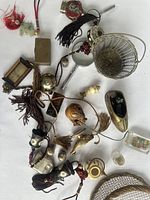 Overview photo of assorted small decorative objects on white surface showing various miniature items including clock, tasselled objects, brass shoe container, metal basket
