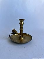 Side view of tarnished brass candle stick showing freestanding structure and attached candle snuffer.