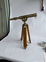 Full view of the brass telescope mounted on a wooden tripod showing the full length and structure.
