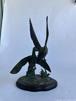 Front view of brown metal duck figurine on wood base displaying two ducks with wings spread in flight or landing pose.