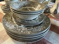 Stack of ceramic plates and bowls showing floral patterned edges and castle central design in brown on white ceramics.