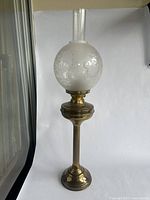 Full view of the metal and frosted glass oil lamp with an etched floral pattern globe