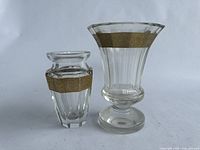 Pair of clear glass vases with embossed gold bands, one taller with flared top, the other shorter with a narrower neck.