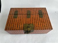Top view of closed rectangular wooden box with Asian script design and metal hinges and latch.