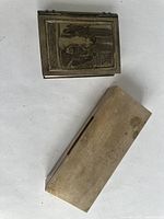 Two silver boxes on a white background, one smaller with engraving and one larger rectangular box