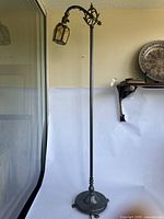 Full view of the approximately 54-inch tall metal floor lamp with curved arm and glass lantern shade in amber tone, standing against a wall.