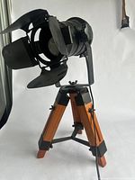 Front angled view of the industrial style table lamp showing the spotlight head with barn doors and wooden tripod base.