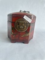 Side view of wooden hexagonal box showing brass latch and painted decoration of Chinese figures and motifs.