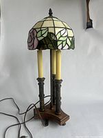 Full view of the vintage stained glass table lamp showing floral stained glass shade in pink, green and cream, metal base with three vertical columns, and faux candle-style bulbs.