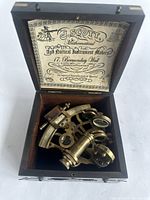Brass sextant inside fitted wooden case, showing instrument position and interior label