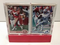 Photo showing both Joe Montana and Barry Sanders Upper Deck football cards side by side in plastic holders with a red base.