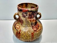 Front view of a ceramic decorative vase showing its multicolor abstract design in brown, red, and beige, with two handles on either side near the neck.