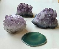 Photo showing three amethyst crystal clusters and one polished agate slice on a white background.