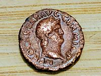 Front view of ancient metal coin showing bust of male figure with inscriptions on edge.