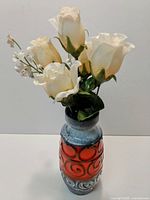 Front view of ceramic vase with the artificial flower arrangement inside, showing white roses and greenery