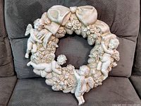 Full frontal view of the ceramic wreath showing four cherubic angels, floral details and a large bow on top.