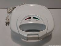 Front of electric sandwich maker showing power and ready indicator lights with cord and plug.