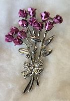 Front view of the vintage floral brooch showing purple flowers, silver leaves, stems, and a bow detail at the bottom