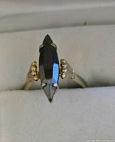Front view of fashion ring with a large marquise-shaped black stone set vertically in a gold-tone setting.