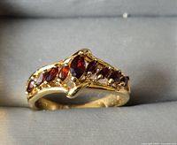 Photo showing front view of the gold tone ring with nine red gemstones arranged across the band.