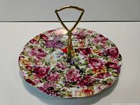 Top view of a medium-sized floral porcelain serving plate with a gold-tone metal handle in the center.