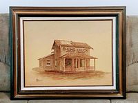 Framed artwork depicting a wooden building with sign 'CHUNG CHUCK POTATO SCHOOLS'. Sepia-toned etching or painting in a wood frame, placed on fabric background.