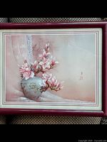 Framed print showing floral artwork in soft pink tones with plastic frame and face.