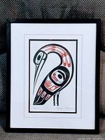 Framed print displayed against a dark textured fabric, showing the stylized bird artwork and the black metal frame.