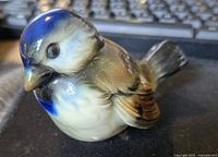 Front view of the glossy porcelain bird figurine showing blue head, white face, and brown detailed wings.